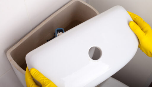 Overhead view of a person wearing rubber gloves removing the lid of a toilet tank.