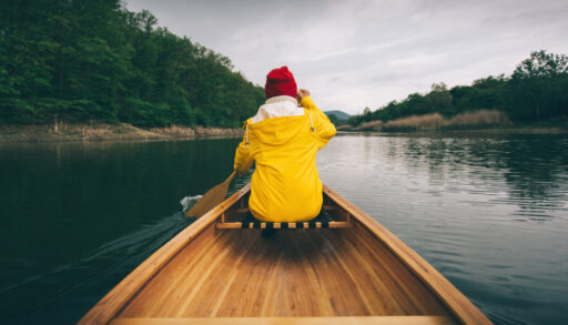 Rear view of a woman in a yellow jacket paddling a canoe.