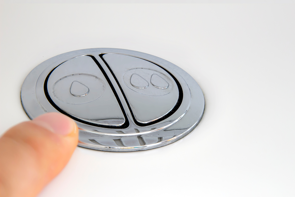 Finger above a low-flow toilet flush button.