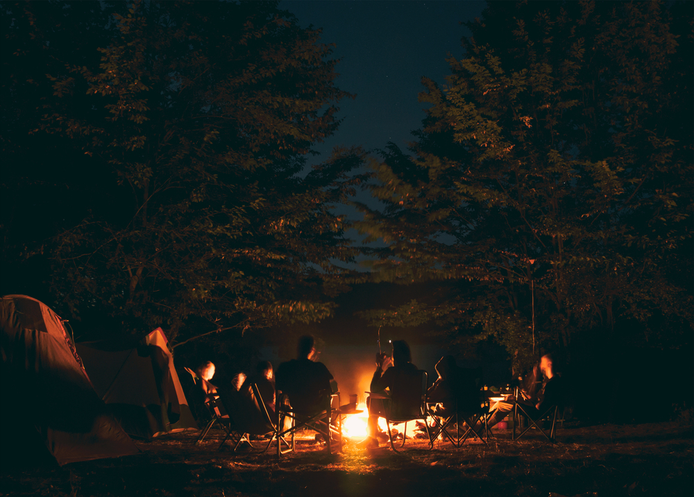 Individuals sitting around burning campfire in forest