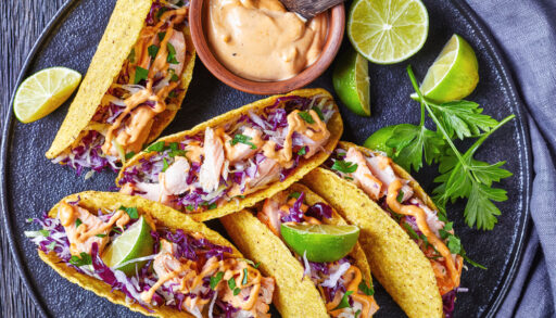 Overhead view of a plate of fish tacos with lime, cilantro and a spicy sauce.