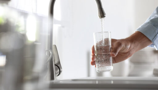 Person filling a glass of water from a faucet.