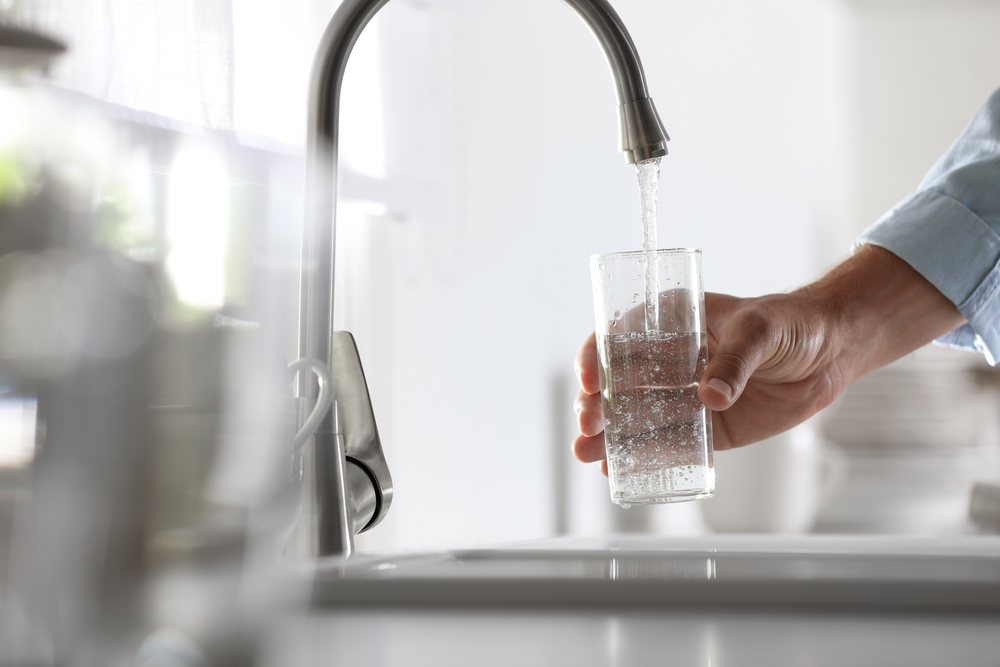 Person filling a glass of water from a faucet.