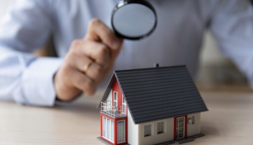 Man holding a magnifying glass looking at a small cottage.