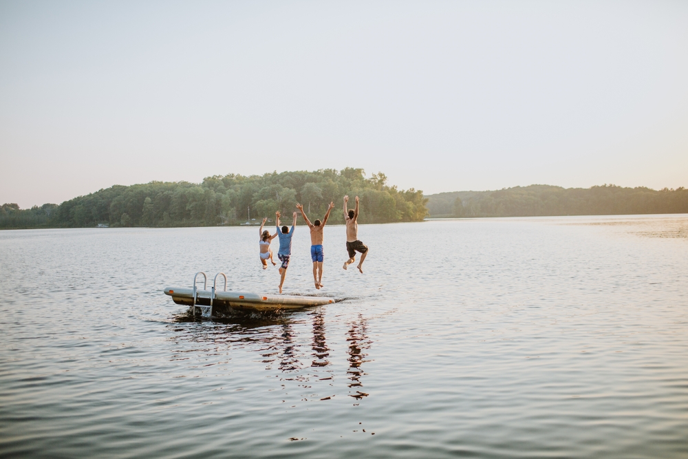 Kids jumping off a floating dock into a lake.