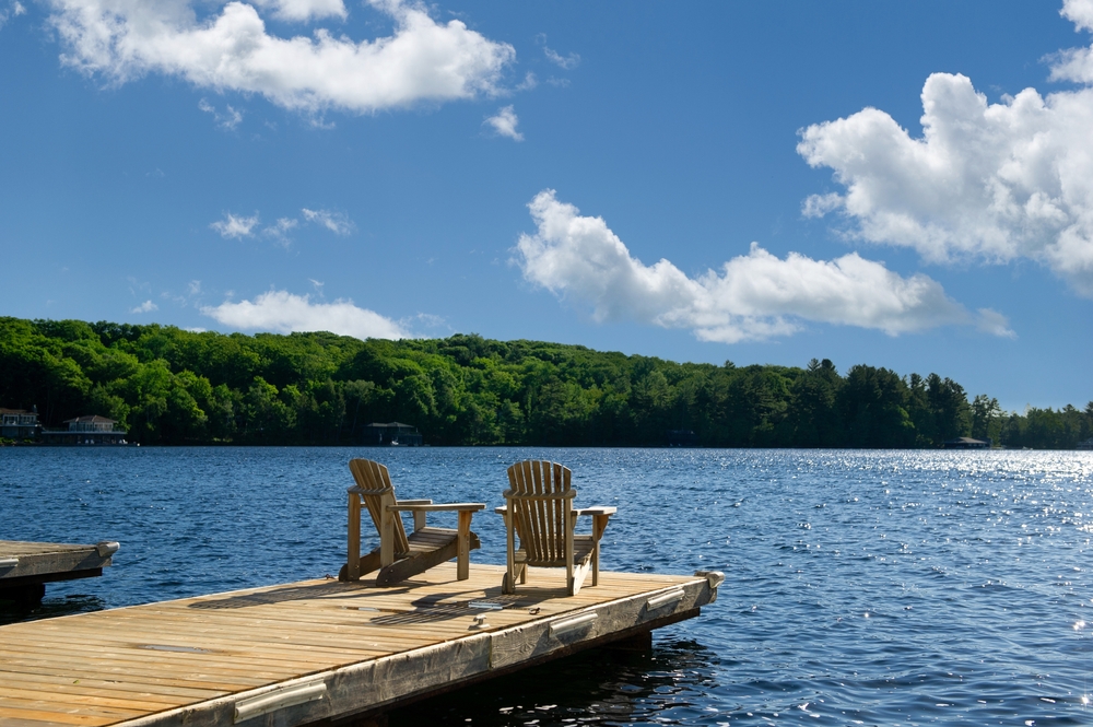 Muskoka chairs on a dock overlooking a lake.