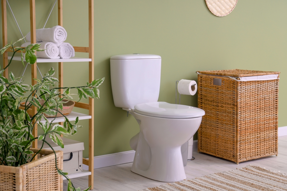 Toilet in a green bathroom next to a wicker basket and shelf.