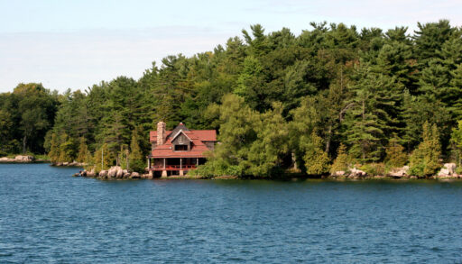 Red waterfront cottage surrounded by green trees.