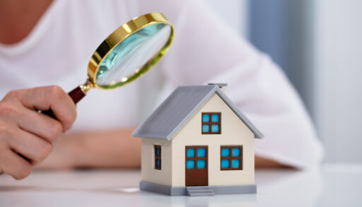 Woman holding a magnifying glass while inspecting a house model.