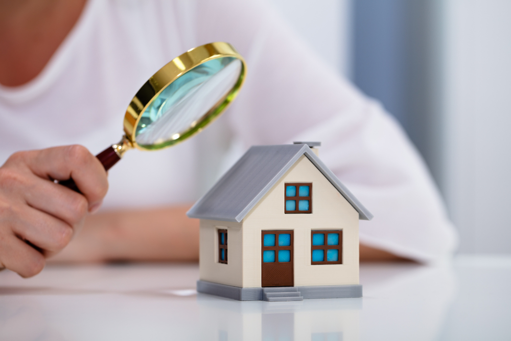 Woman holding a magnifying glass while inspecting a house model.