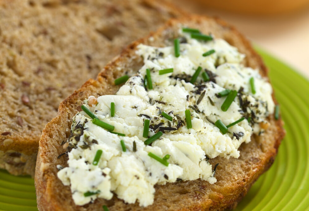 Goat cheese sprinkled with chives spread on wholegrain bread.
