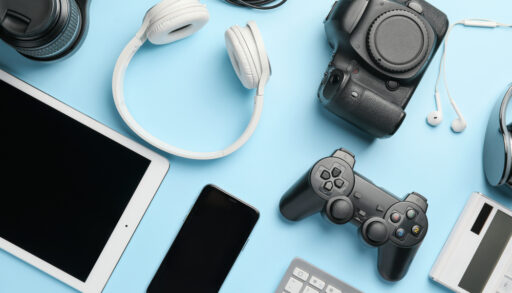 Various electronic devices on a blue background, including game controllers, headphones, smartphones and tablets.