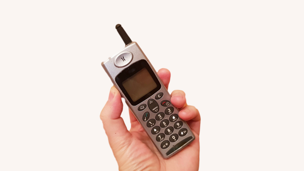 Person holding an old analog cellphone with a small antenna.