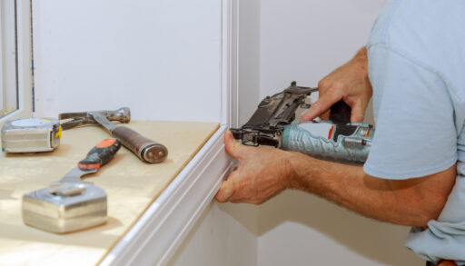 Person installing window trim with a nail gun.