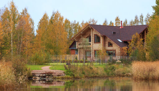 Wooden cabin next to a lake surrounded by autumn trees.