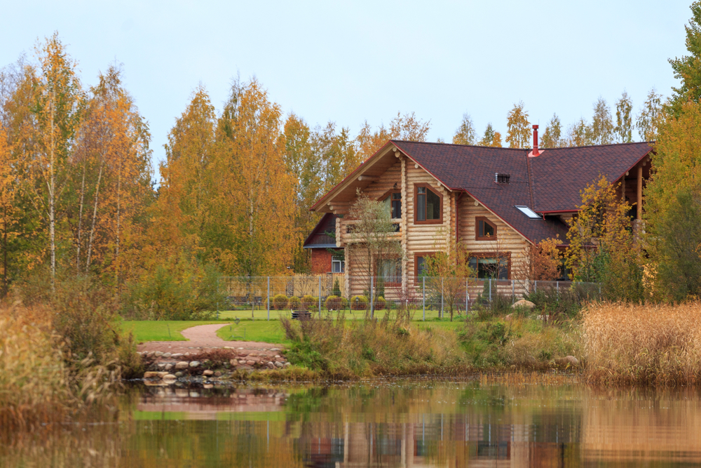 Wooden cabin next to a lake surrounded by autumn trees.