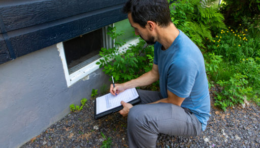 Indoor damp & air quality (IAQ) testing. A close up view on environmental home quality inspector at work, filling in a form as he inspects the exterior of a cellar window, with room for copy.