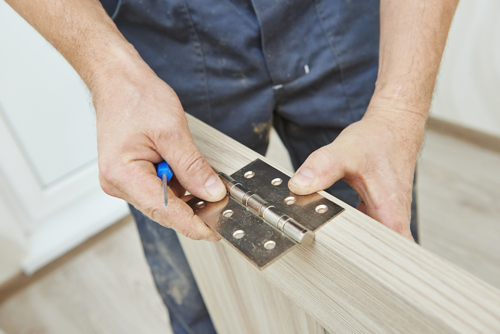 Man putting a metal hinge on a wooden door.