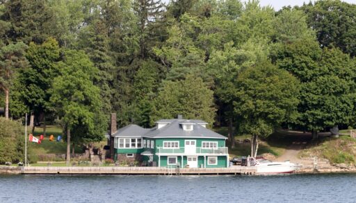 Green two-storey cottage next to a lake.