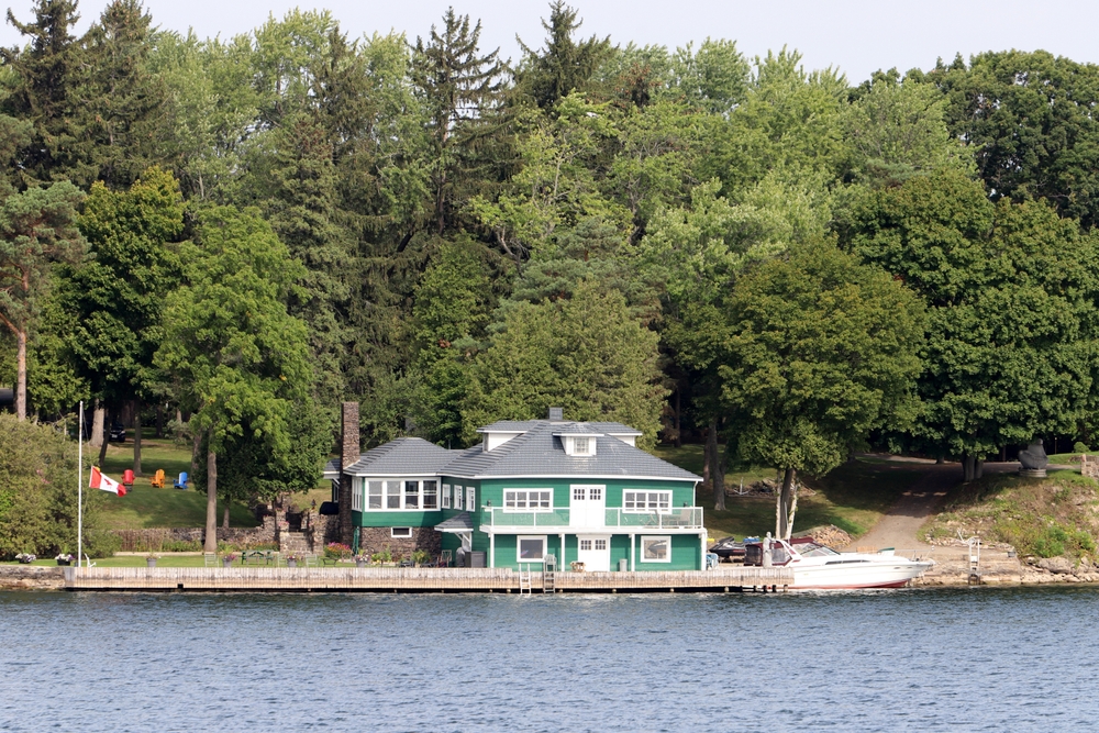 Green two-storey cottage next to a lake.