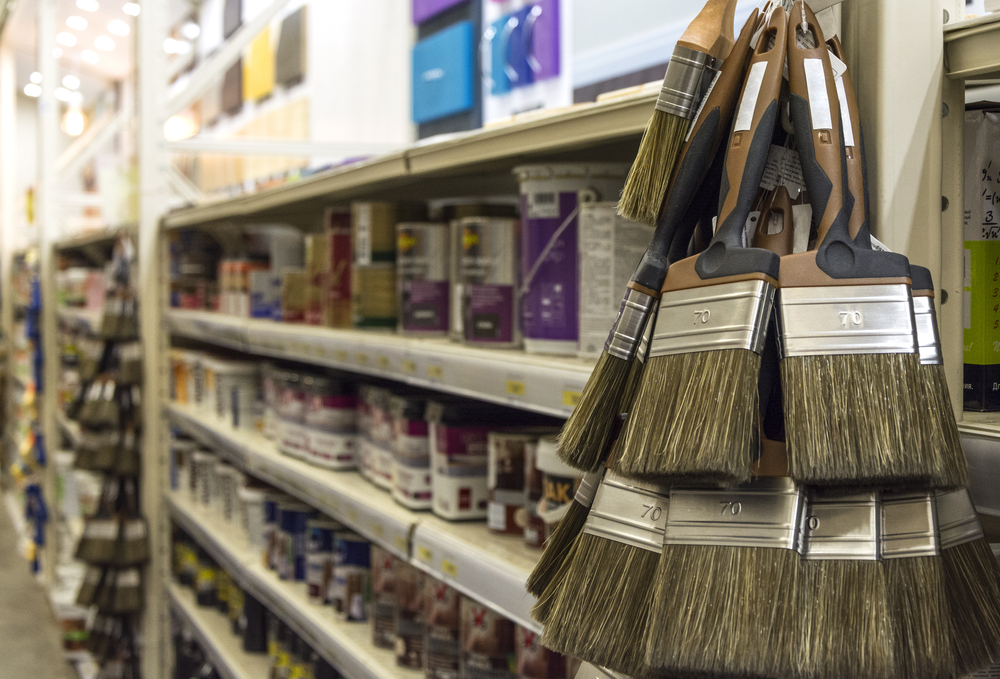 Close-up of paint brushes in front of a shelf of paint cans.