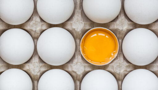 Overhead view of eggs in a carton with one egg cracked in half showing the yolk.