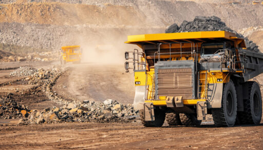 Yellow dump truck carrying sediment out of an open mining pit.
