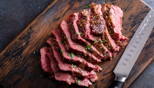 Close-up of sliced corned beef on a wooden cutting board next to a knife.