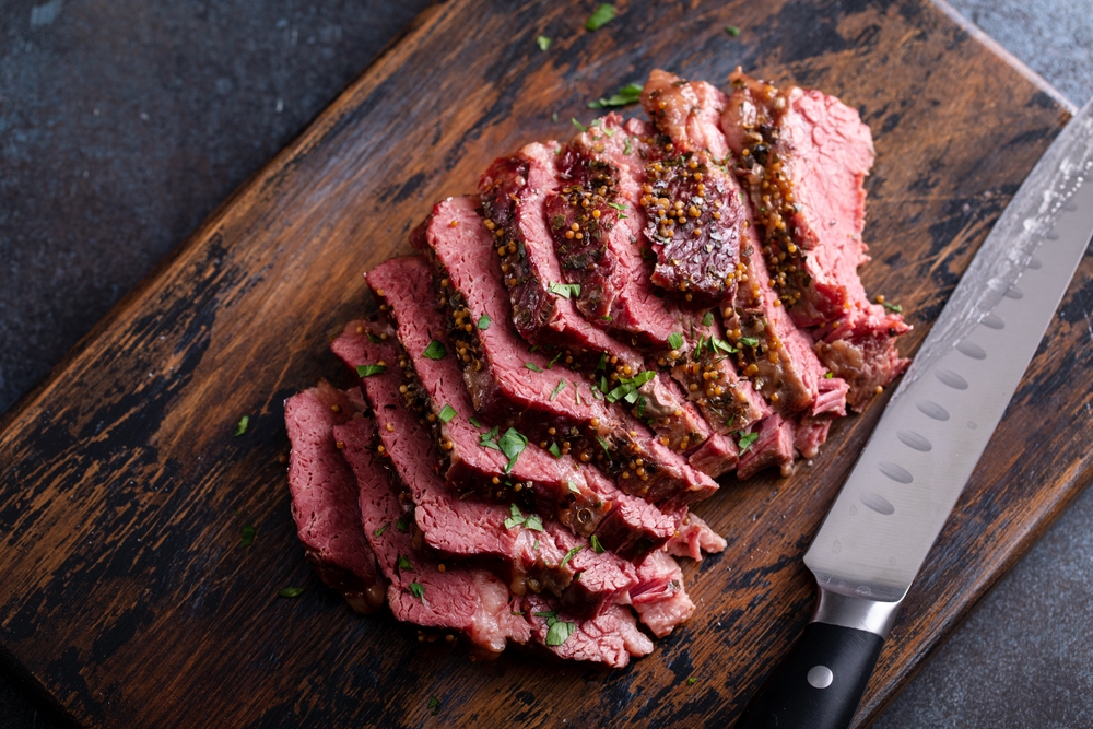 Close-up of sliced corned beef on a wooden cutting board next to a knife.