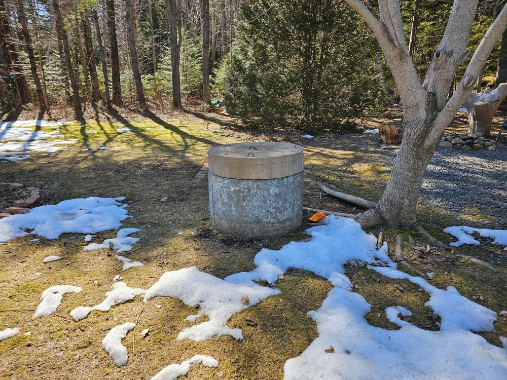 Large dug well underneath a tree on a lawn.