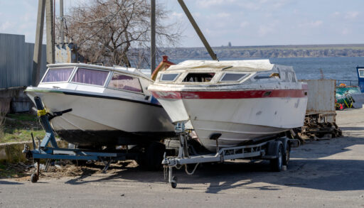 Two used boats parked on the pavement near the water.