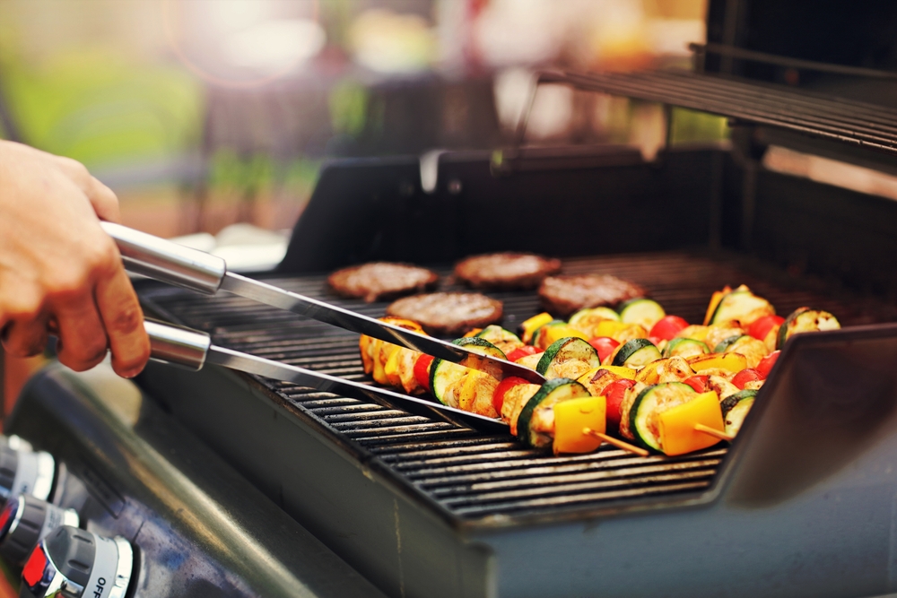 Person using tongs to flip kabobs on a barbecue.
