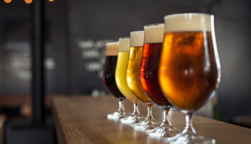 Row of different types of beer in glasses on a wooden countertop.