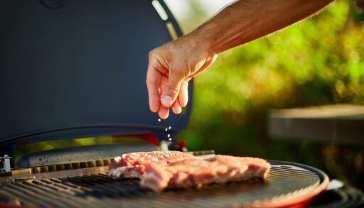 Close-up of a man's hand as he seasons meat on a grill.