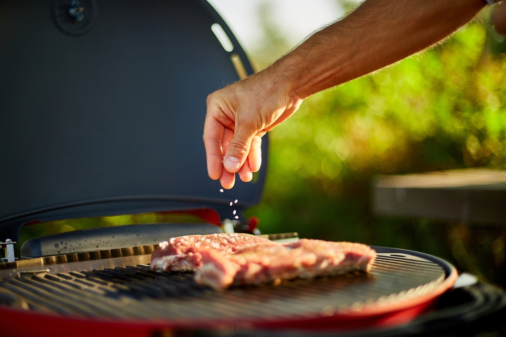 Close-up of a man's hand as he seasons meat on a grill.