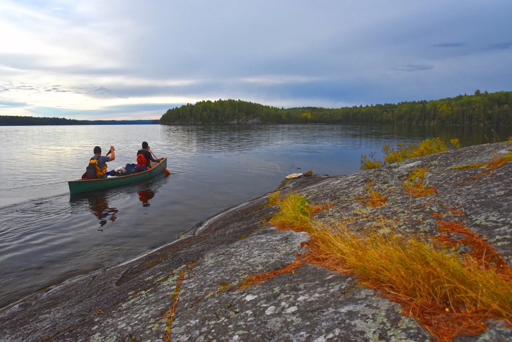 Two people in a canoe paddle Cirrus Lake in Quetico Provincial Park, Ontario.