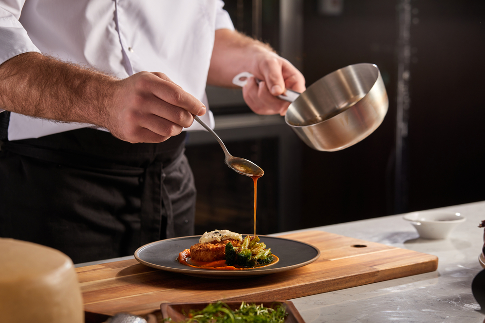 Close-up of a chef pouring a sauce over a plate.