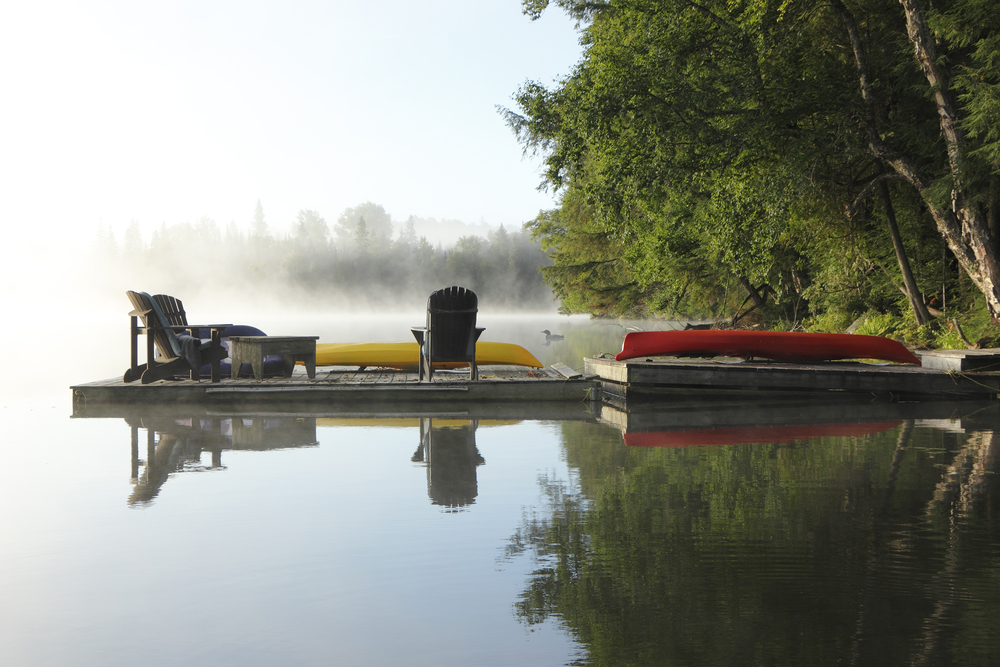 Dock with Muskoka chairs and a canoe on a misty morning in Haliburton, Ontario.