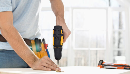 Man wearing a toolbelt using a drill.