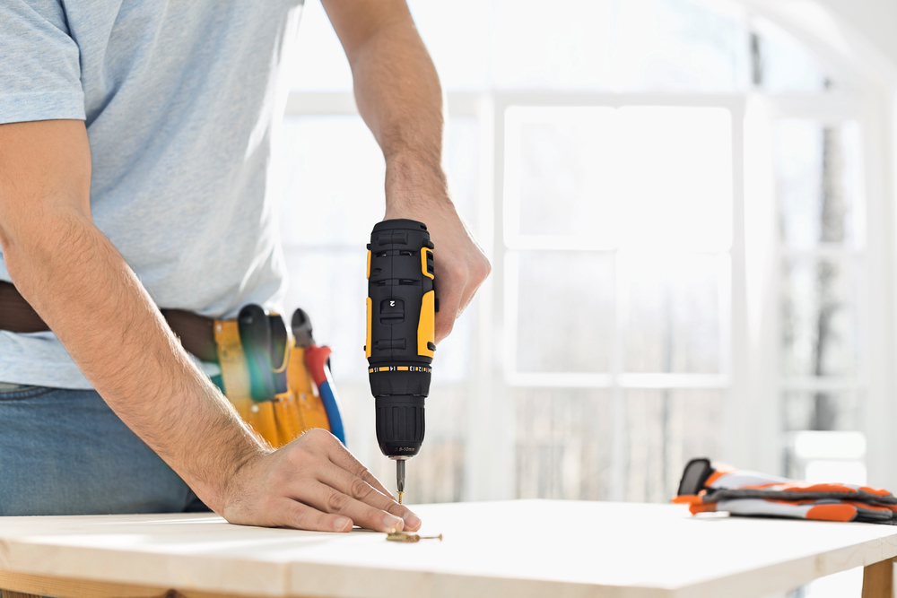 Man wearing a toolbelt using a drill.