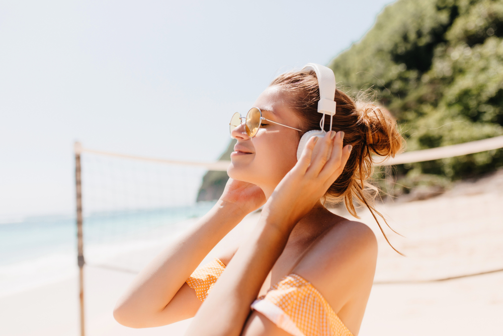 Woman with headphones on listening to music on a beach.