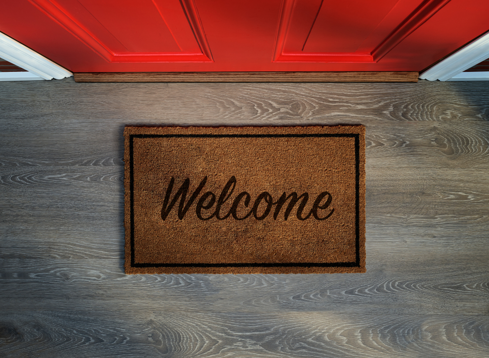 Overhead view of a welcome mat in front of a red door.