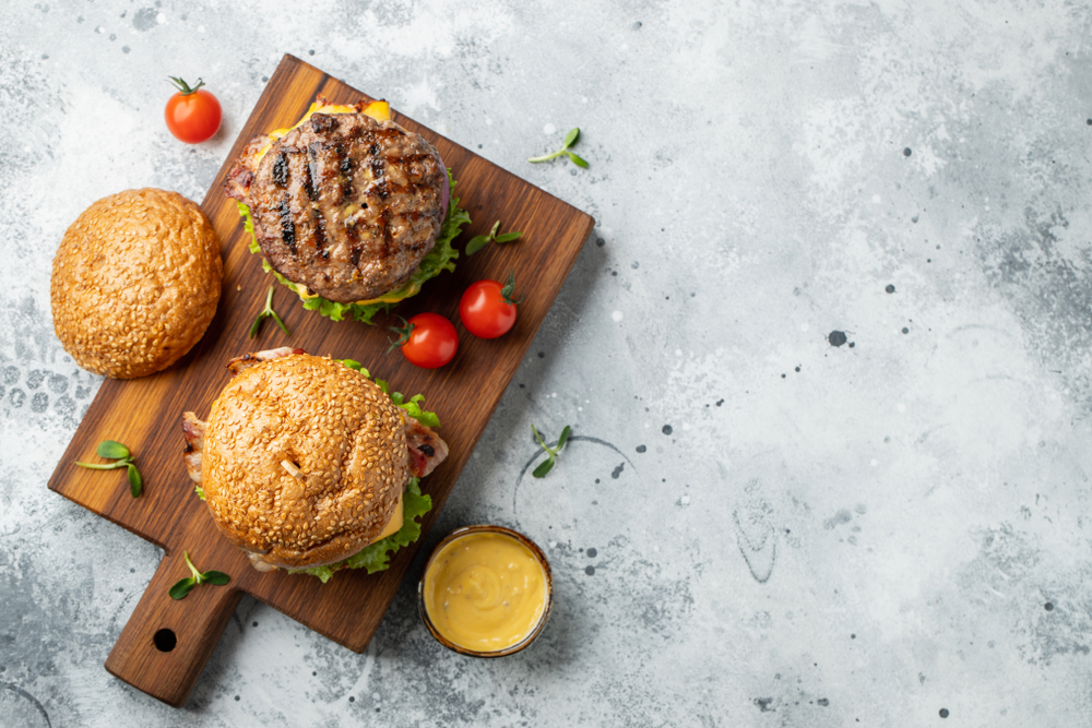 Overhead view of two burgers on a wooden cutting board.