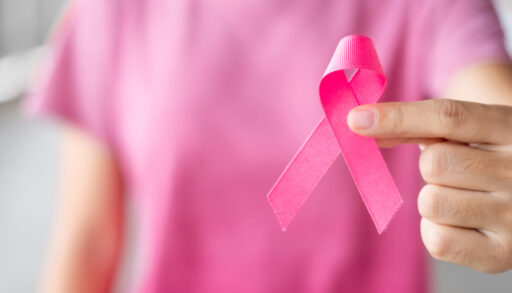 Person in a pink shirt holding a pink ribbon in support of breast cancer.