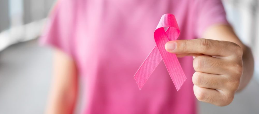 Person in a pink shirt holding a pink ribbon in support of breast cancer.