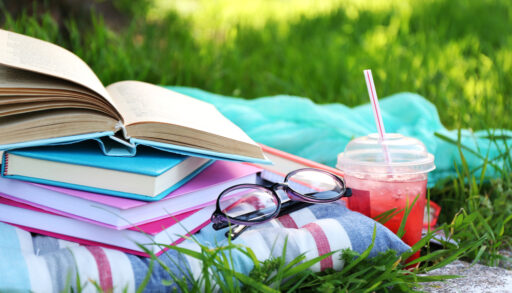 Books laying on top of blankets with reading glasses and a summer drink.