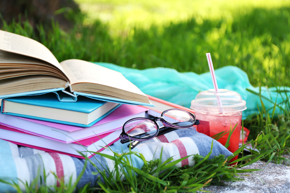 Books laying on top of blankets with reading glasses and a summer drink.