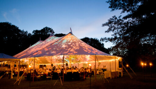 Special event tent lit up from the inside with dark blue night time sky and trees