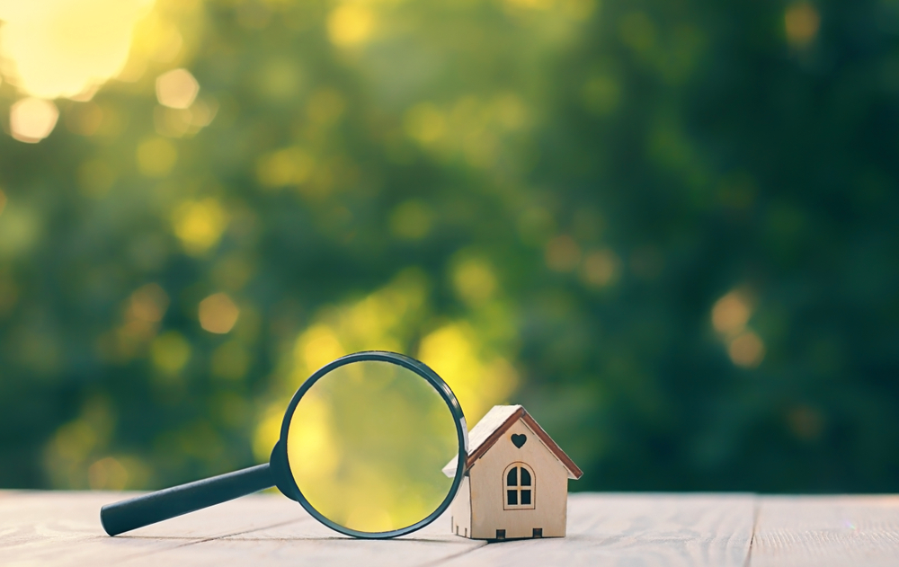 mini house and magnifying glass, natural green background. House searching, choice of location for construction, of mortgage, rental housing.