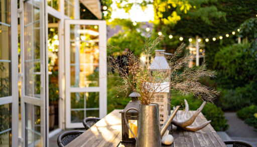 Decorated outdoor table in front of open cottage doors with fairy lights hanging above.